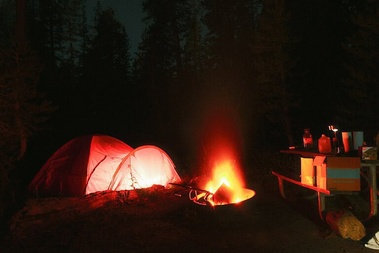 Illuminated tent and campfire at a forest campsite after dark