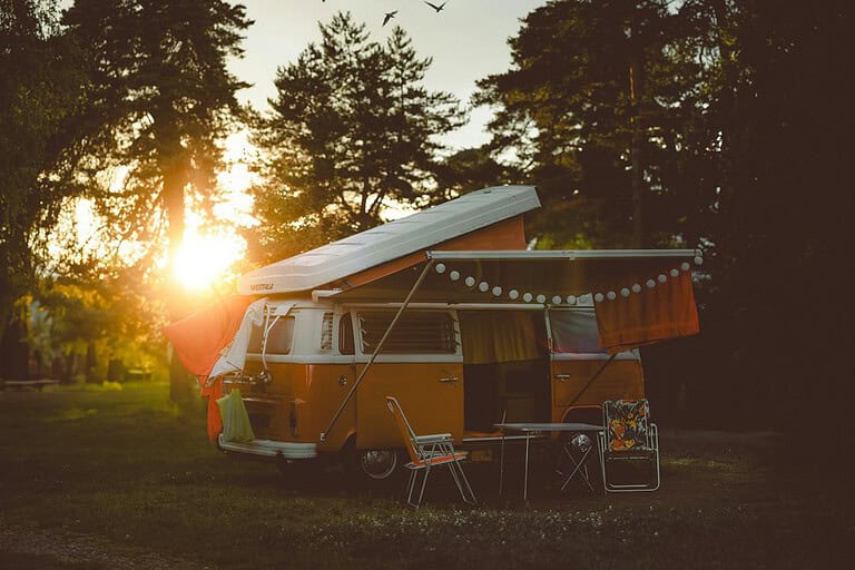 Yellow camper van with an awning at a wooded campsite