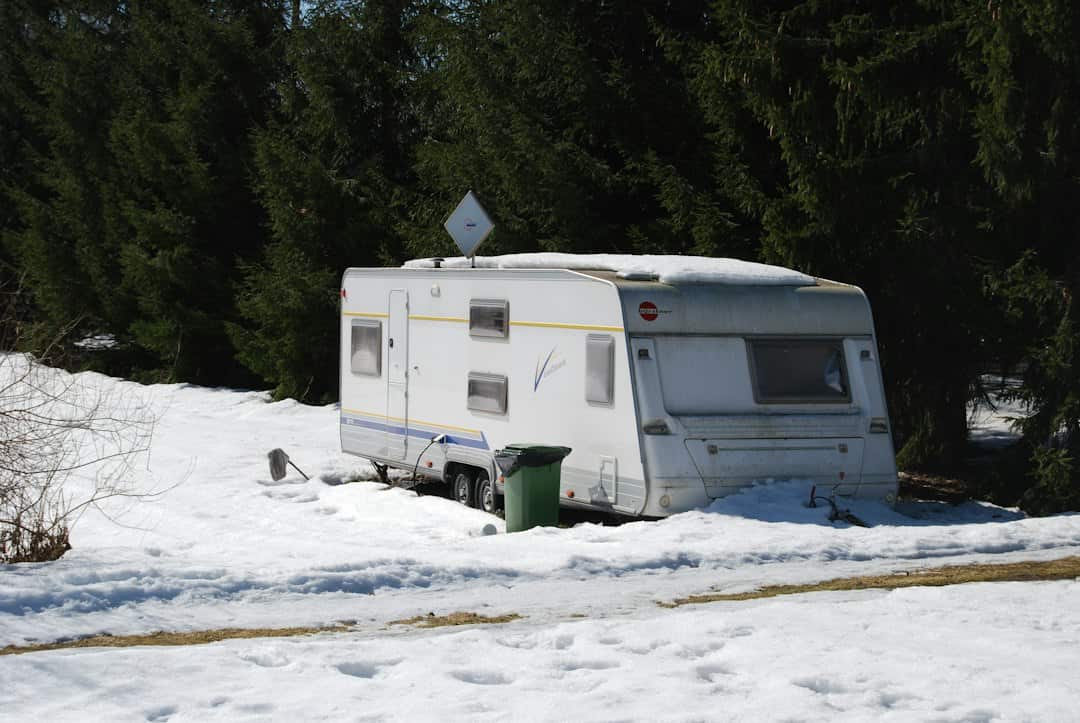 Travel trailer parked in snow beside a forest