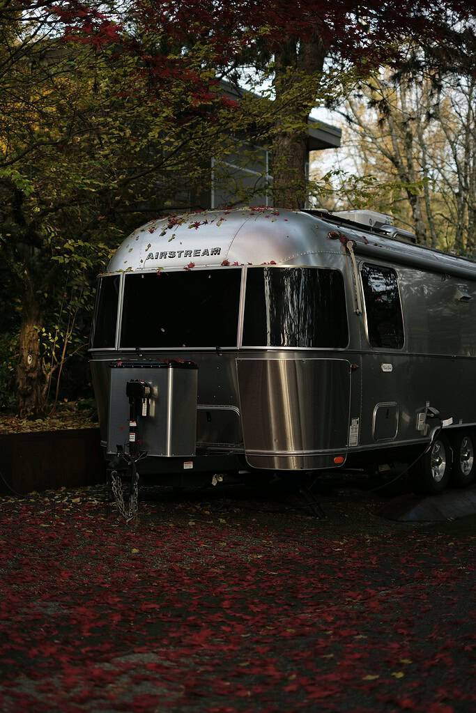Silver travel trailer near trees with autumn leaves in North Vancouver